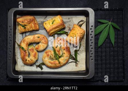 Cibo con cannabis. Torta fatta in casa, decorata con foglie di marijuana verde in un piatto da forno su marmo nero Foto Stock