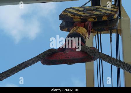 Vista sul gancio in acciaio rosso della gru da carico della nave fissata tramite una fune sul ponte principale. Foto Stock