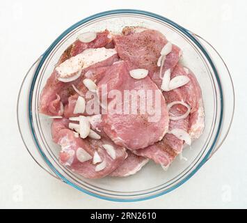 Maiale crudo a fette cosparso di pepe e cipolla tritata in un recipiente di vetro. Vista dall'alto, primo piano. Foto Stock