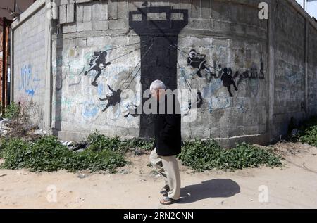 (150227) -- GAZA, 27 febbraio 2015 -- Un palestinese cammina davanti a un murale di bambini usando una torre di guardia dell'esercito israeliano come un giro in altalena, dipinta dall'artista di strada britannico Banksy, sui resti di una casa distrutta durante l'offensiva israeliana di 50 giorni sulla Striscia di Gaza negli ultimi luglio e agosto, nella città settentrionale di Beit Hanun, nella Striscia di Gaza, il 27 febbraio 2015.) MIDEAST-GAZA-MURALS-BANKSY YasserxQudih PUBLICATIONxNOTxINxCHN Gaza febbraio 27 2015 un PALESTINESE cammina davanti a un murale di bambini che usa la torre di guardia dell'esercito israeliano come un giro in slitta che ha dipinto il British Street Artist Banksy o Foto Stock