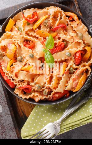 Mafaldine di pasta italiana cucinata con salsa di pomodoro cremosa con capperi, basilico e peperoni da vicino in una ciotola sul tavolo. Vista dall'alto verticale da ab Foto Stock