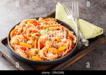 Reginette con peperoni e basilico in salsa di pomodoro cremosa con primi piani di capperi sul piatto sul tavolo. Orizzontale Foto Stock