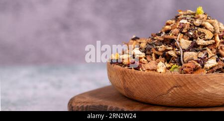 Tè invernale secco. Foglie di tè invernali essiccate al sole in un recipiente di legno. Tè invernale preparato con mela granulata, limone, arancia, zenzero, galangal, melissa, rosem Foto Stock