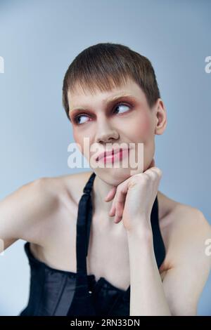 persona queer con trucco che guarda lontano su un modello grigio, androgino, espressione di sé, scettico Foto Stock