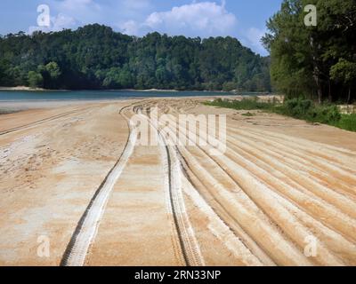 La prospettiva delle piste dei pneumatici dei veicoli 4x4 è stata vista sulla sabbia dorata, le jeep hanno guidato lungo l'ampia spiaggia sabbiosa, il mare delle Andamane, le verdi montagne e il cielo blu i. Foto Stock