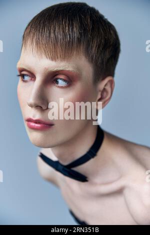 modello queer con trucco che guarda dall'altra parte, sfondo grigio, moda, papillon, androgino, ritratto Foto Stock