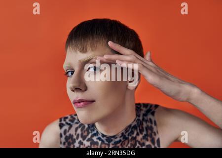 persona androgina sorridente e guardante la fotocamera su sfondo arancione, volto toccante, moda queer Foto Stock