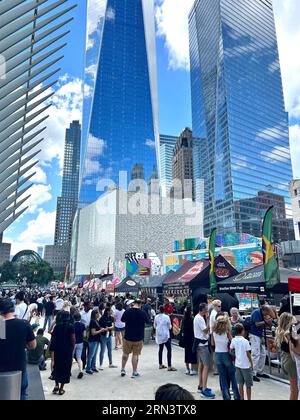 Newyorkesi e turisti fuori dall'Oculus Center sulla plaza con la Freedom Tower e altri edifici dietro e un grande gruppo di venditori di cibo che offrono una varietà di cucine. Foto Stock