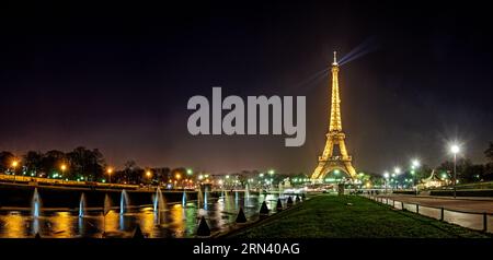 PARIGI, Francia: La Torre Eiffel si erge illuminata contro il cielo notturno della capitale francese. L'iconica struttura in ferro si illumina di luci dorate e il suo brillante display crea un faro nel paesaggio notturno parigino. Foto Stock