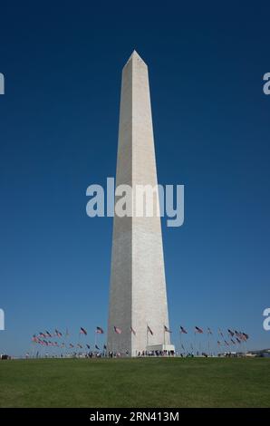 Washington Monument American Flags Washington DC | WASHINGTON D.C., Stati Uniti - i visitatori si riuniscono alla base del Washington Monument, inghiottito da bandiere americane, sul National Mall. Completato nel 1884 su progetto di Robert Mills, l'obelisco in marmo di 555 piedi (169 m) onora George Washington e rimane la struttura in muratura più alta del mondo. Foto Stock
