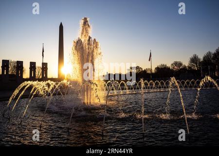 World War II Memorial Fountain Washington DC // WASHINGTON DC - la fontana al centro del National World War II Memorial cattura la luce del sole appena dopo l'alba, con il Washington Monument visibile in lontananza. La piscina arcobaleno del monumento funge da fulcro della piazza di 7,4 acri (3 ettari) che onora i 16 milioni di americani che hanno servito durante la seconda guerra mondiale. Dedicato nel 2004, il monumento presenta 56 colonne di granito che rappresentano gli stati e i territori degli Stati Uniti, disposte in un semicerchio intorno alla fontana cerimoniale. Foto Stock