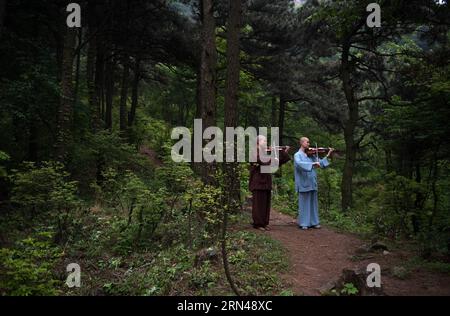 Due monaci praticano il violino in un bosco nel tempio di Tiantai nella contea di Hong An, provincia di Hubei nella Cina centrale, 6 maggio 2015. I monaci del Tempio di Tiantai sono competenti non solo nel dharma del Buddha, ma anche negli strumenti orchestrali. Il Maestro Wule ha iniziato a ricostruire il Tempio di Tiantai, vecchio di 1400 anni, dal 2004. Come ex musicista, organizzò l'orchestra monaca Guangxuan per predicare il buddhismo e la filosofia Zen attraverso la musica nel 2008. I membri dell'orchestra imparano a suonare strumenti da zero e a superare numerose difficoltà. Attirando credenti e monaci che si identificano con l'idea del pra buddista Foto Stock