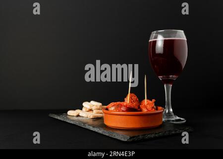 Chorizo iberico, salsiccia iberica, fritta in vaso di argilla con pane e vino rosso tipico tapa spagnolo isolato su fondo nero e spazio copia Foto Stock