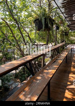 La terrazza in legno con la lunga panca e piante tropicali per rilassarsi al secondo piano nella casa di campagna, vista frontale con lo spazio fotocopie. Foto Stock