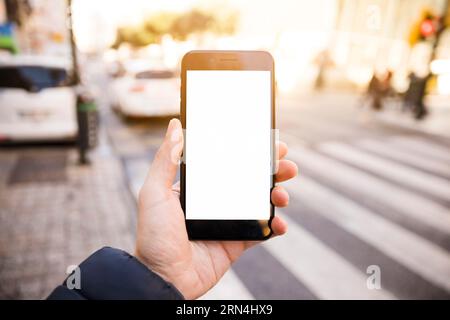 Primo piano della mano dell'uomo che mostra il telefono cellulare con schermo bianco sulla strada Foto Stock