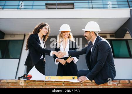 Architetti che indossano caschi che stringono le mani Foto Stock