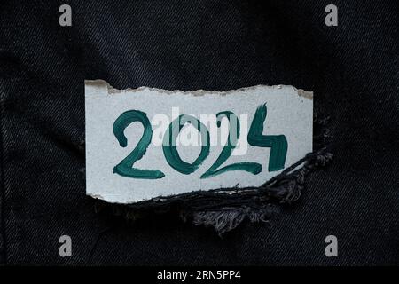 il 2024 è scritto con vernici verdi su un cartoncino di carta che si trova su denim nero, felice anno nuovo 2024, banner e sfondo Foto Stock