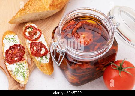 Pomodori secchi in olio d'oliva in un vaso di vetro e panini pronti sul tavolo Foto Stock