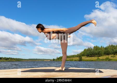 Una donna che conduce uno stile di vita sano e pratica yoga esegue l'esercizio Virabhadrasana, la posa numero tre guerriero, si allena in abbigliamento sportivo su t Foto Stock