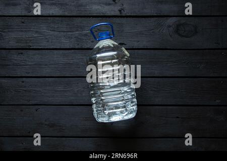 Una bottiglia d'acqua di plastica da cinque litri si trova su un asse di legno nero, acqua in bottiglia Foto Stock