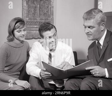 1960s INSURANCE SALESMAN SHOWING DISCUSSING PORTFOLIO TO COUPLE IN THEIR LIVING ROOM - s12893 HAR001 HARS COPY SPACE HALF-LENGTH LADIES PERSONS MALES B&W PARTNER SELLING DISCUSSING OCCUPATIONS MID-ADULT MID-ADULT MAN MID-ADULT WOMAN SALESMEN WIVES BLACK AND WHITE CAUCASIAN ETHNICITY HAR001 OLD FASHIONED PORTFOLIO Stock Photo