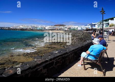 Coppia che si rilassa su una panchina con vista sul mare, Playa Blanca, Lanzarote e le isole Canarie. Preso il 23 febbraio Foto Stock