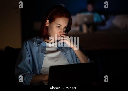 Donna freelance che lavora al buio di un notebook a casa guardando lo schermo. Foto Stock