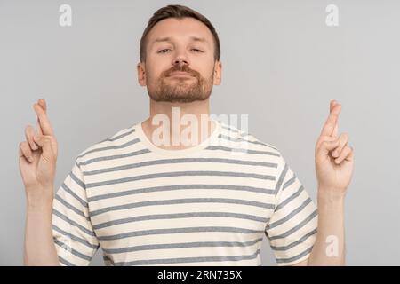 Uomo soddisfatto con le dita incrociate segno di buona fortuna in attesa di momento sfondo isolato studio. Foto Stock