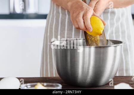 Le mani del cuoco grattugiano la scorza di limone in un recipiente di impasto. Sapore naturale in scorza di limone vidi. Preparare gli ingredienti in una panetteria o in un ristorante ki Foto Stock