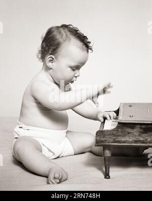 1940s BABY WEARING A CLOTH DIAPER WITH SAFETY PINS SITTING PLAYING A TOY PIANO - b19917 HAR001 HARS BRUNETTE PERFORMING ARTS DISCOVERY DIAPERS OCCUPATIONS MUSICAL INSTRUMENT GROWTH INTENSE JUVENILES PIANIST TALENT BABY GIRL BLACK AND WHITE CAUCASIAN ETHNICITY HAR001 INTENT OLD FASHIONED PIANOS Stock Photo