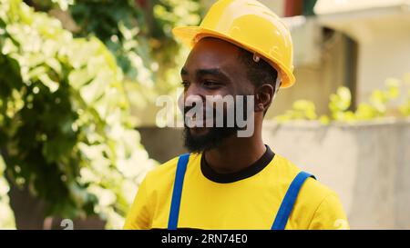 Revealing shot of smiling repairman happy with freon levels in outdoor condenser while using manometer to accurately measure HVAC system pressure, ensuring optimal cooling performance and efficiency Stock Photo