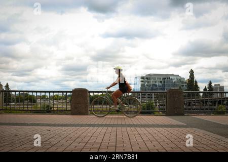 Donna in bicicletta lungo il fiume Willamette nel Tom McCall Waterfront Park di Portland, Oregon Foto Stock