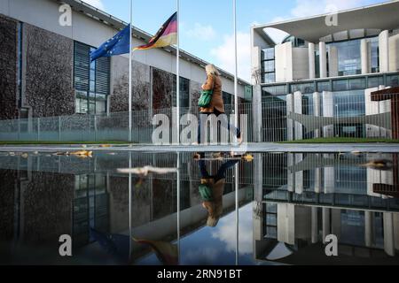 (151114) -- BERLINO, 14 novembre 2015 -- Una donna cammina come bandiera dell'UE e una bandiera nazionale tedesca sventola a mezz'asta alla Cancelleria di Berlino, Germania, il 14 novembre 2015. Oltre 100 persone sono state uccise in un sequestro di massa in una sala concerti di Parigi venerdì e molte altre sono state temute morte in una serie di bombardamenti e sparatorie. ) GERMANY-BERLIN-PARIS-ATTACK-CONDOOLENCE Zhangxfan PUBLICATIONxNOTxINxCHN 151114 Berlino Nov 14 2015 una donna cammina come bandiera UE e una bandiera nazionale tedesca vola A mezz'asta ALLA Cancelleria di Berlino Germania IL 14 novembre 2015 oltre 100 celebrità sono state UCCISE in un ostaggio di massa Foto Stock