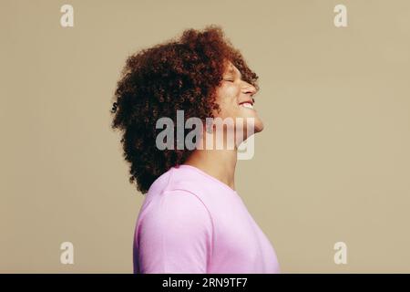 SideView di un giovane con capelli ricci di zenzero e pelle lentigginata che celebra la sua bellezza unica in uno studio. Bell'uomo che sorride felicemente mentre esprime Foto Stock