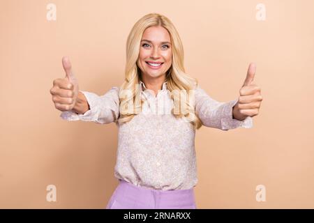 Ritratto di un'affascinante signora che indossa abiti da ufficio casual e intelligenti che sollevano i pollici su uno sfondo di colore beige isolato Foto Stock