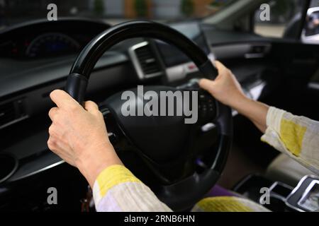 Cropped image of senior woman hands steering wheel of a car while driving . Retired people, road trip and life insurance concept Stock Photo