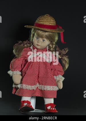 Bambola in tessuto tedesco vintage, bionda dagli occhi blu con trecce in un cappello di paglia con un cappello a nastro rosso e un abito rosso con pois bianchi Foto Stock