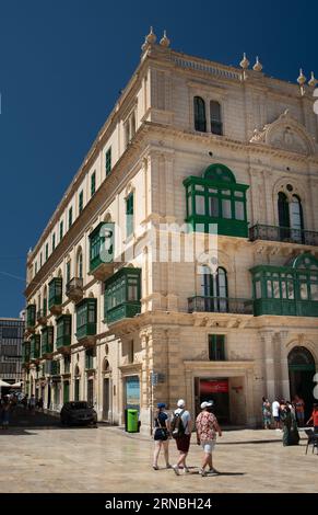 Un gruppo di turisti passeggia attraverso la città vecchia di Valletta a Malta. Sul lato la facciata di un edificio storico con balconi tradizionali. Foto Stock