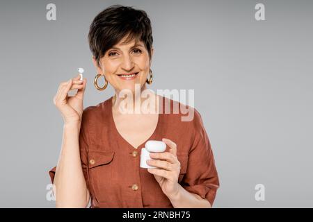donna di mezza età con giacca di lino marrone che regge la custodia per le cuffie con un look autunnale grigio alla moda Foto Stock