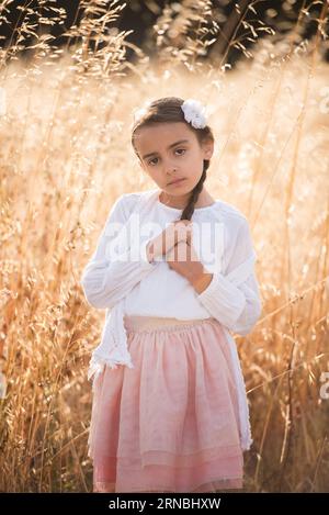 Little girl with braid in white top pink skirt in field of wheat Stock Photo