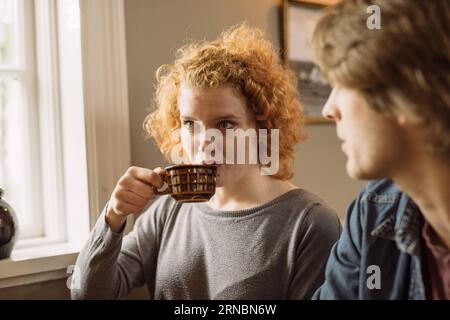 Young woman drinking coffee while sitting with crop friend Stock Photo