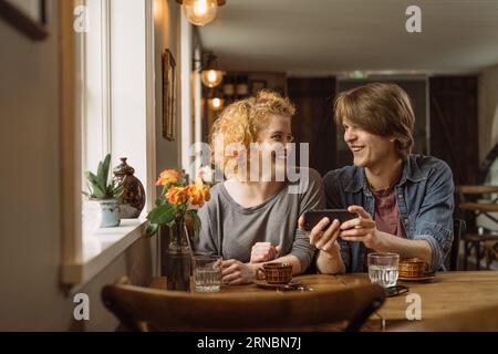 Coppia felice che usa lo smartphone mentre si siede al tavolo con un caffè Foto Stock