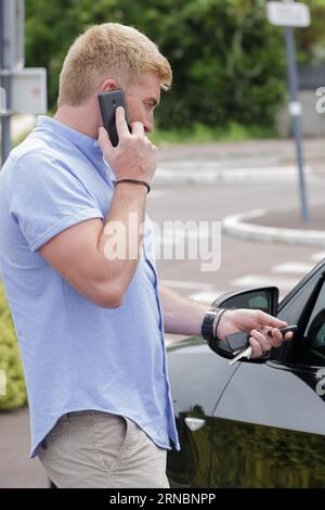 uomo al telefono mentre utilizza la chiave di chiusura centralizzata con telecomando Foto Stock