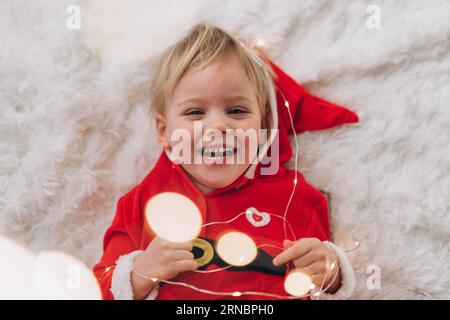 Una bambina bionda in costume di Babbo Natale mente e ride Foto Stock