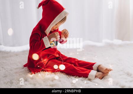 Un bambino vestito con un costume di Babbo Natale siede e guarda le luci Foto Stock