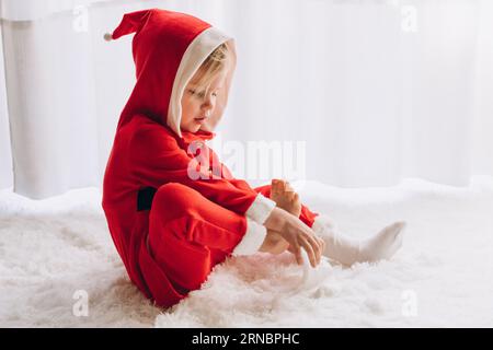 Bambino vestito da Babbo Natale siede e indossa le calze Foto Stock