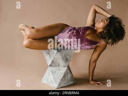 La ballerina nera posa in studio su un elegante sgabello grigio Foto Stock