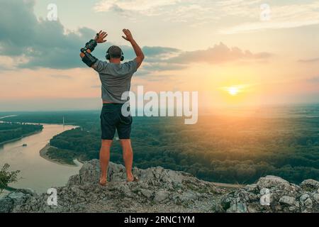 Uomo con ortosi regolabile del gomito articolato sulla scogliera in cima al tramonto Foto Stock