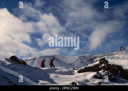 Trekking per due uomini attraverso paesaggi montani innevati in Islanda Foto Stock