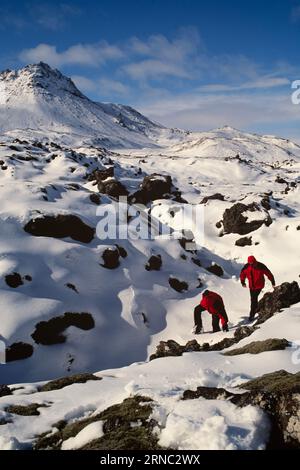 Trekking per due uomini attraverso paesaggi montani innevati in Islanda Foto Stock